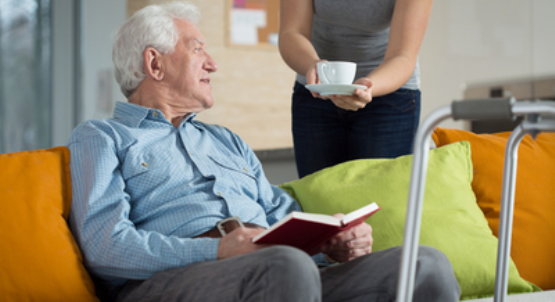 Älterer Mann mit Rollator liest auf dem Sofa